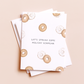 A stack of white greeting cards with a pattern of watercolor bagels and the text 'LET'S SPREAD SOME HOLIDAY SCHMEAR' on a light beige background.