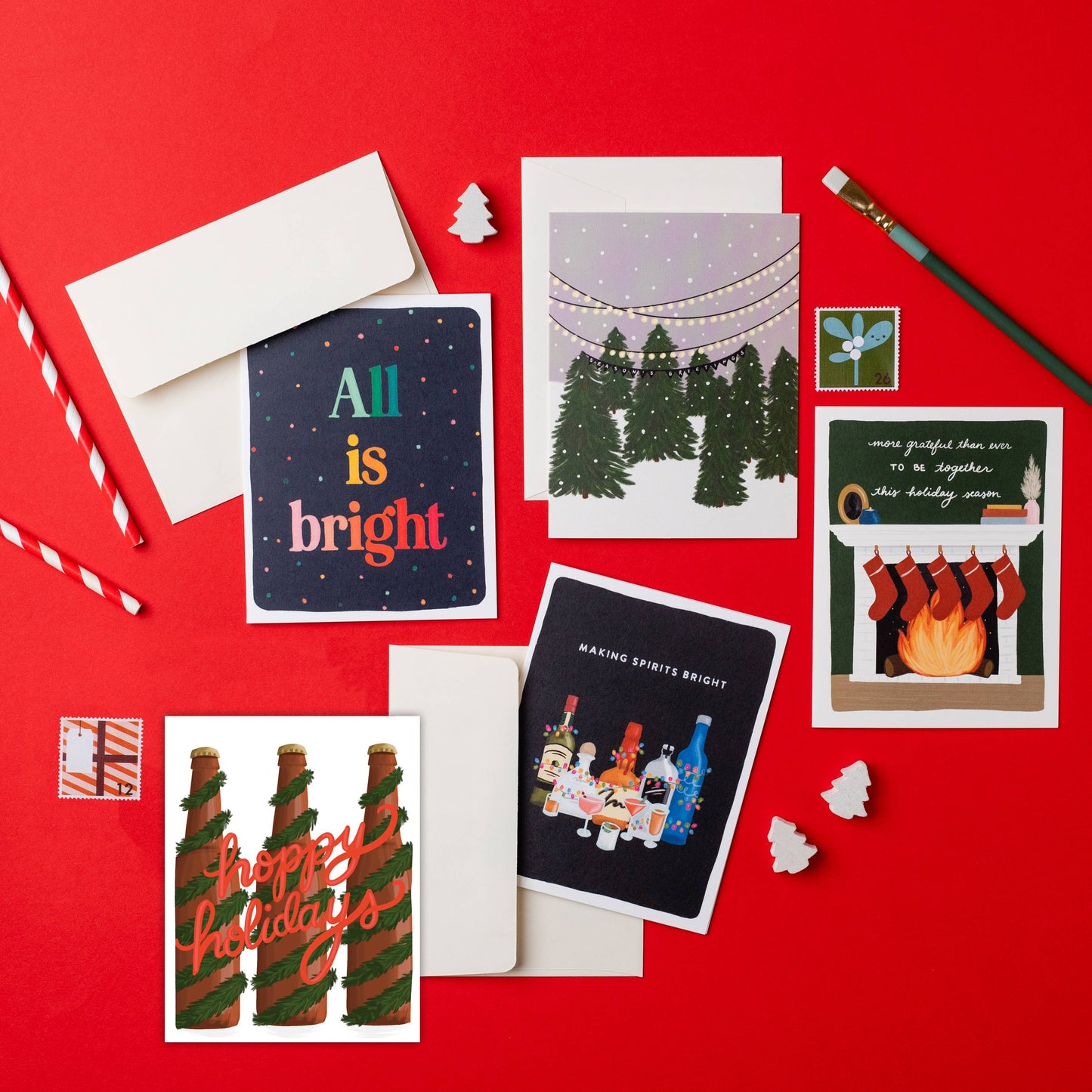 5 different holiday cards scattered on a red backdrop with pencils, erasers and stamps.