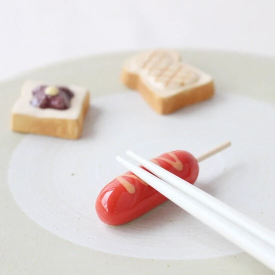 Mini chopstick holder that looks like a hotdog on a stick with mustard drizzle.
