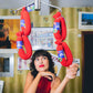 Woman in a red dress standing in front of a counter with hanging socks that look like chorizo links 