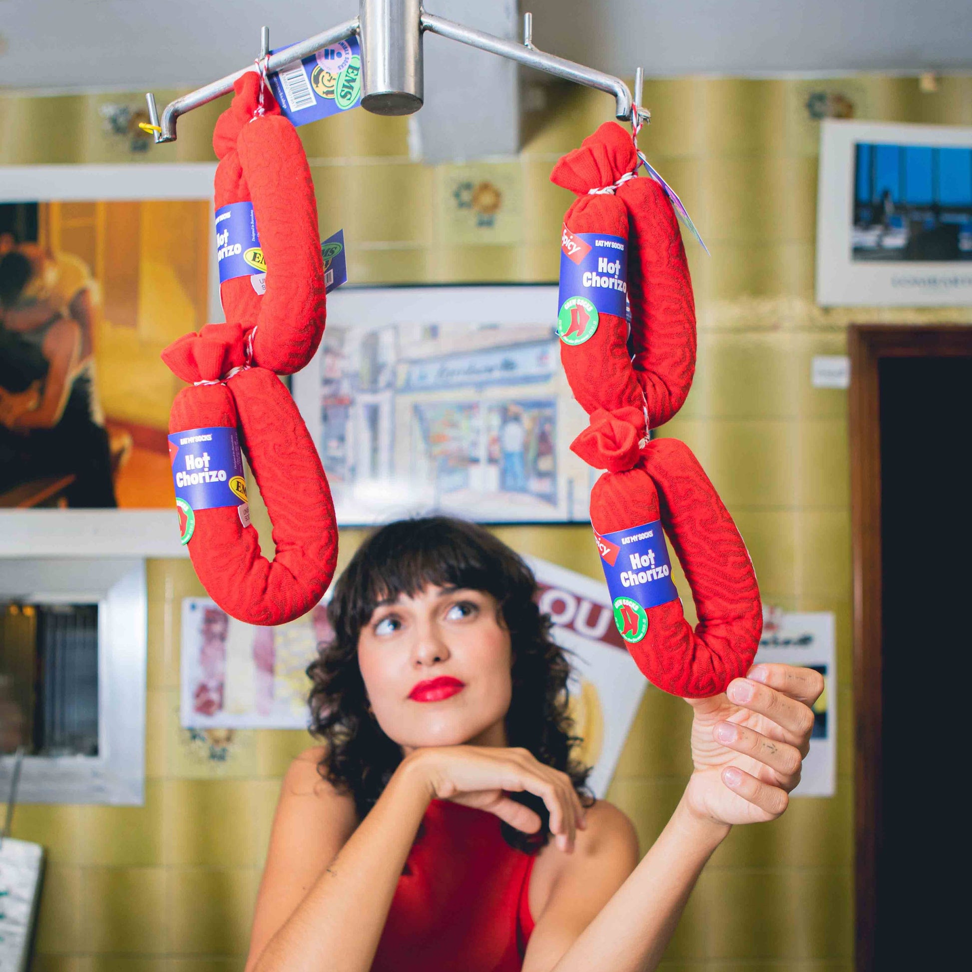 Woman in a red dress standing in front of a counter with hanging socks that look like chorizo links 