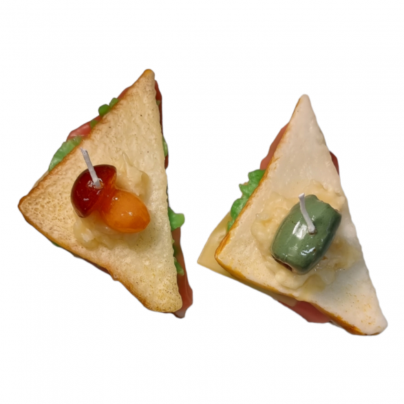 Two wax candles, each shaped like a half sandwich. One has a brown-ish mushroom garnish and the other has a pimento stuffed olive garnish. Both are shaped like triangles.