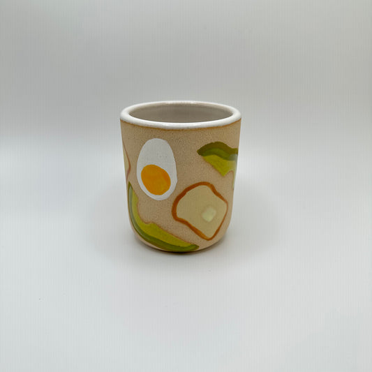 Ceramic Tumlber with hard boiled eggs, avocados and toast with pads of butter hand painted on.