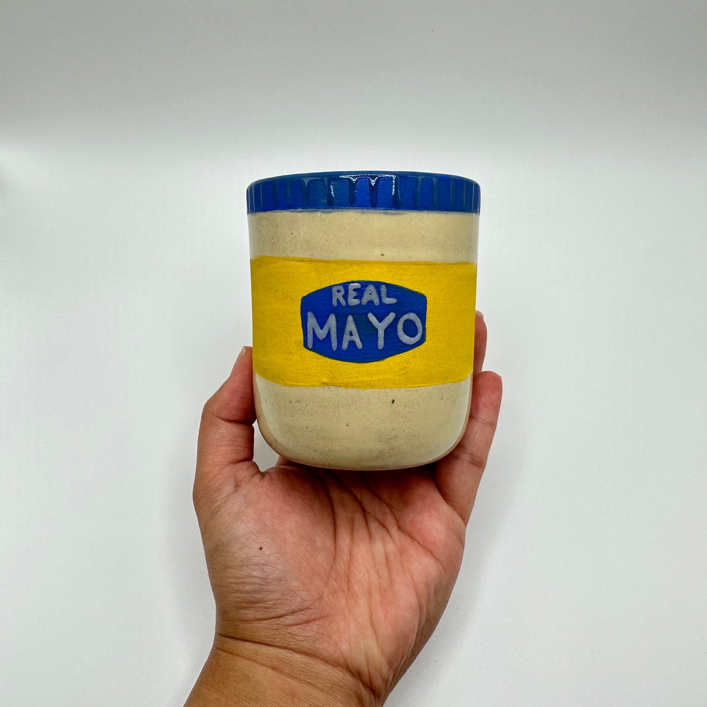 Ceramic tumbler hand painted to look like a jar of "Real May" with a blue lid.