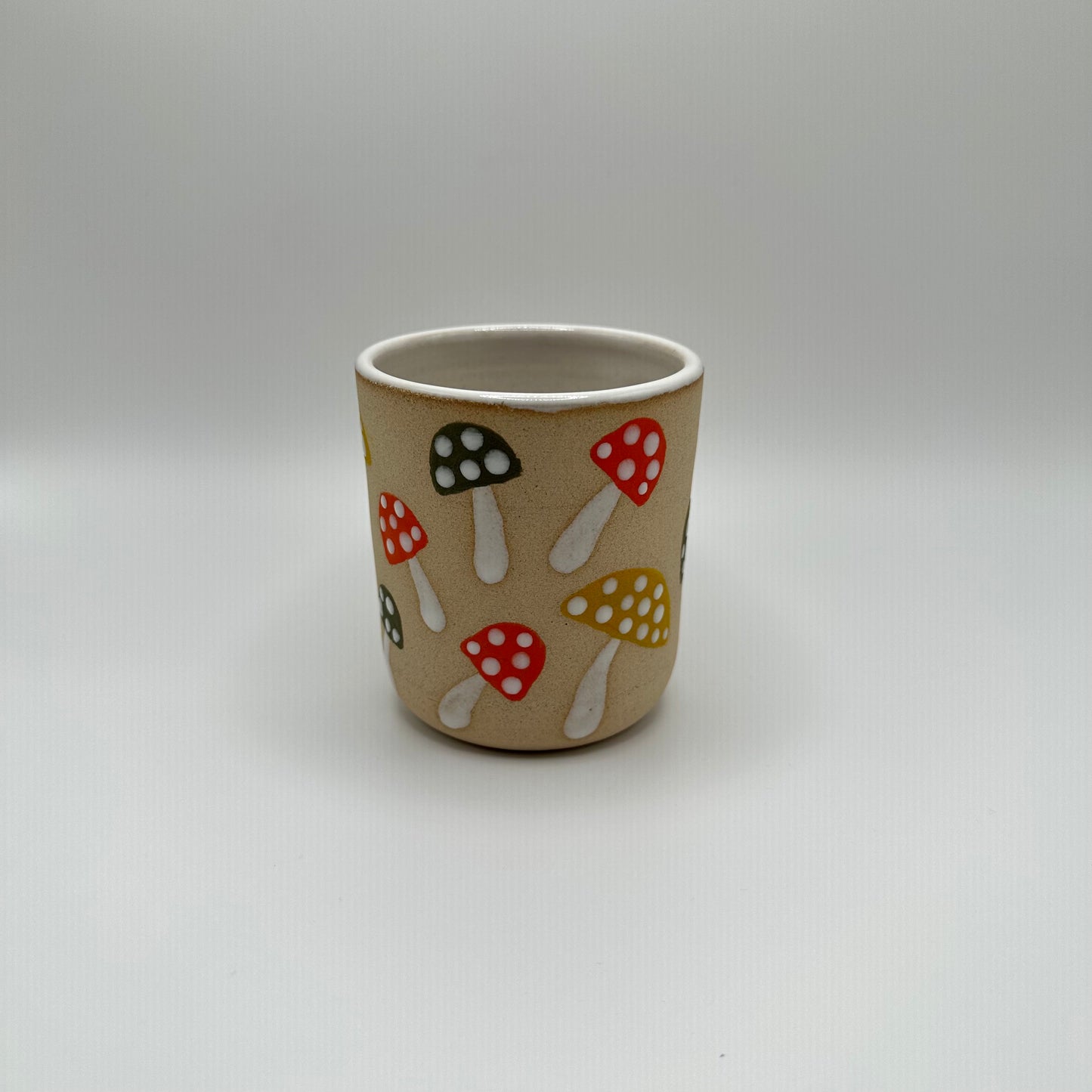 Ceramic tumbler hand painted with various mushrooms in mustard, green, and orange with white stems and white dots on the caps.