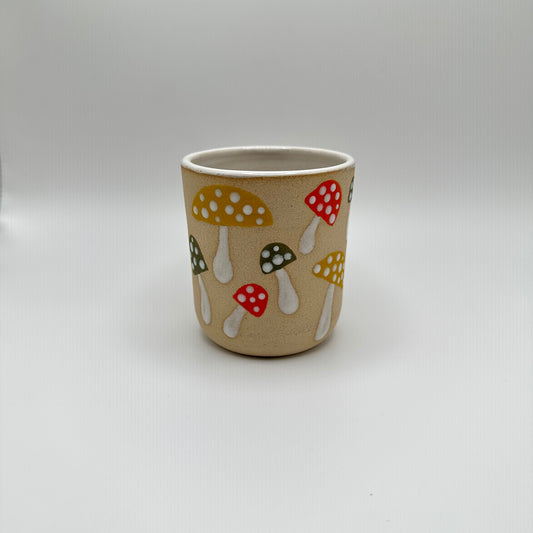Ceramic tumbler hand painted with various mushrooms in mustard, green, and orange with white stems and white dots on the caps.