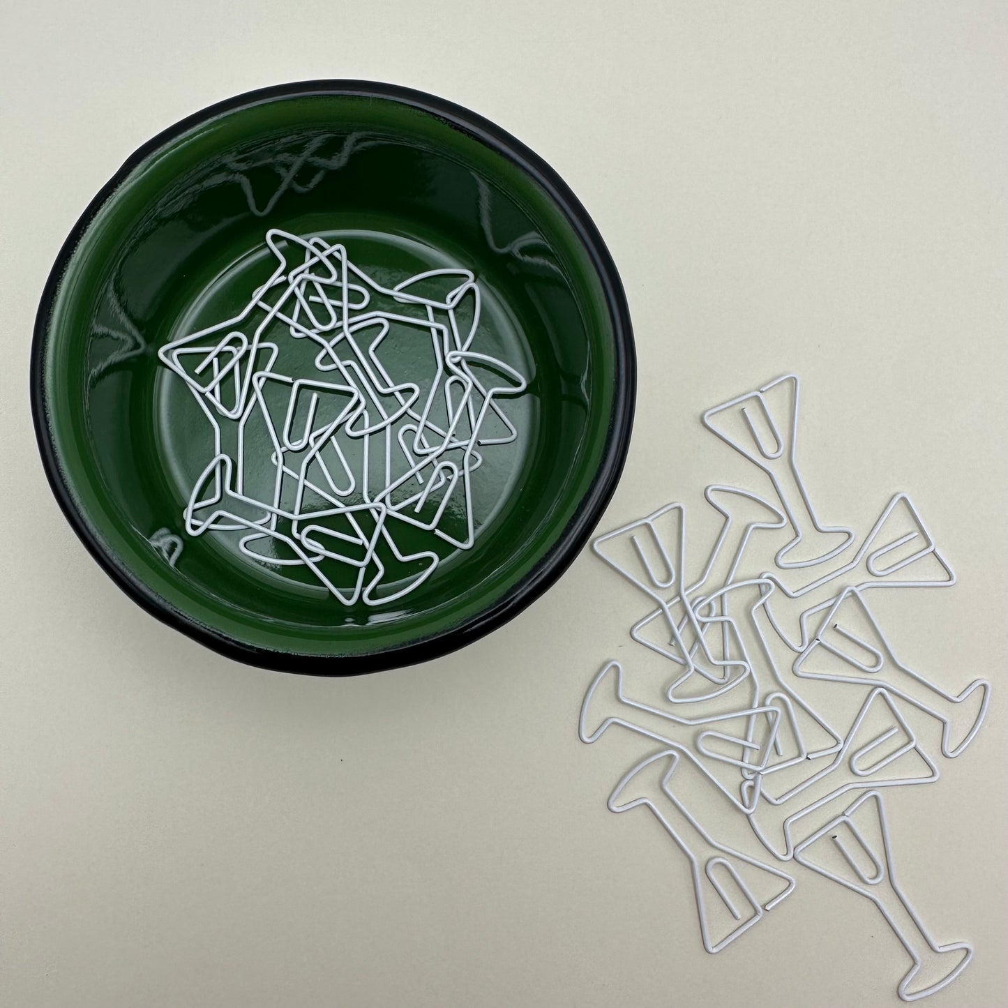 a pile of martini paperclips on the table and in a green ramekin.