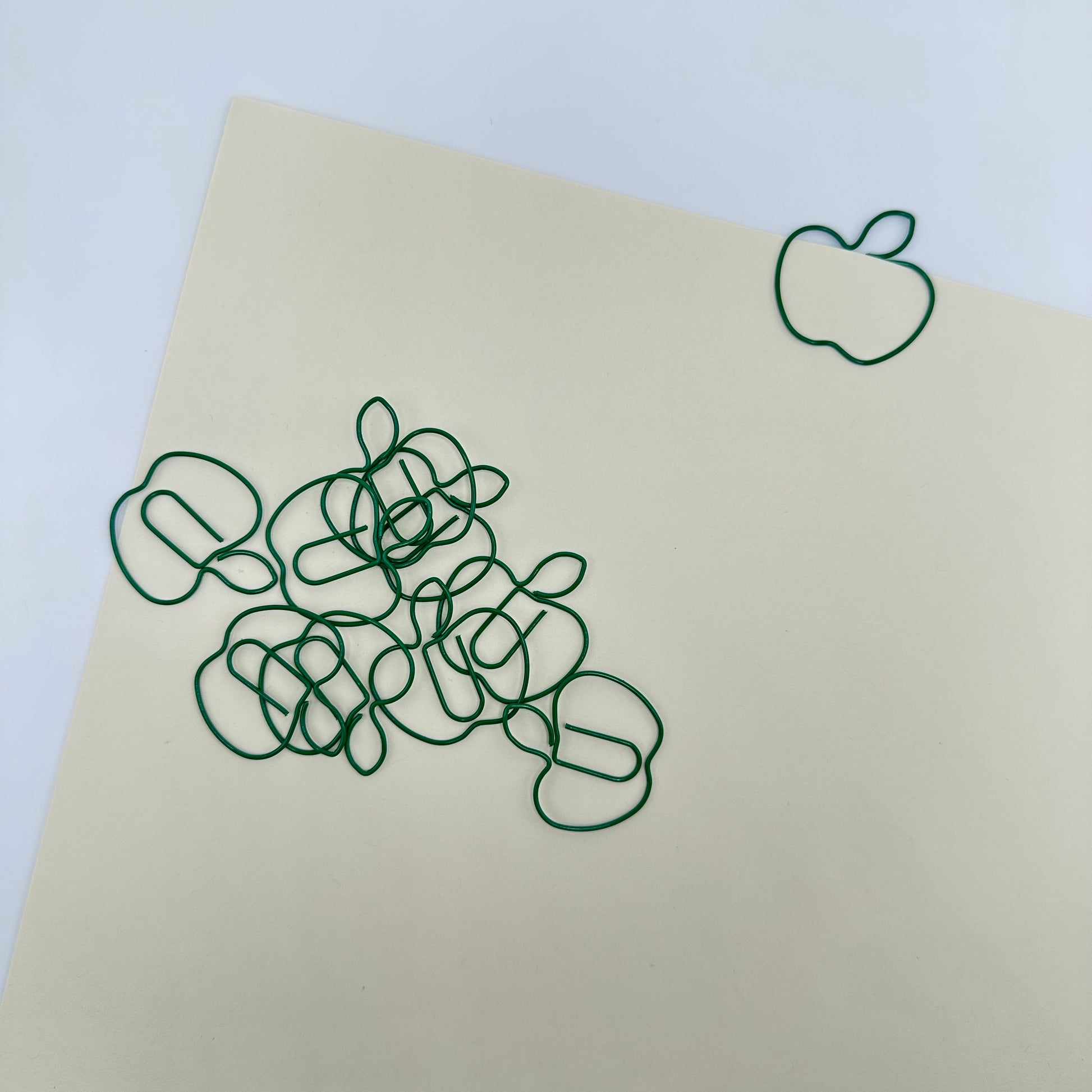 Pile of green apple paperclips on a cream piece of paper.