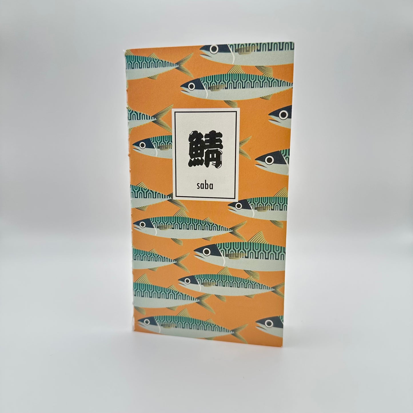 Orange notebook with mackerel in a pattern. Box with Japanese characters that read Saba.