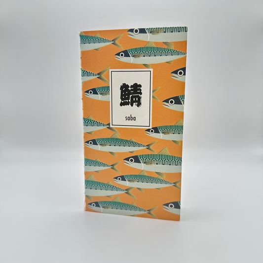 Orange notebook with mackerel in a pattern. Box with Japanese characters that read Saba.