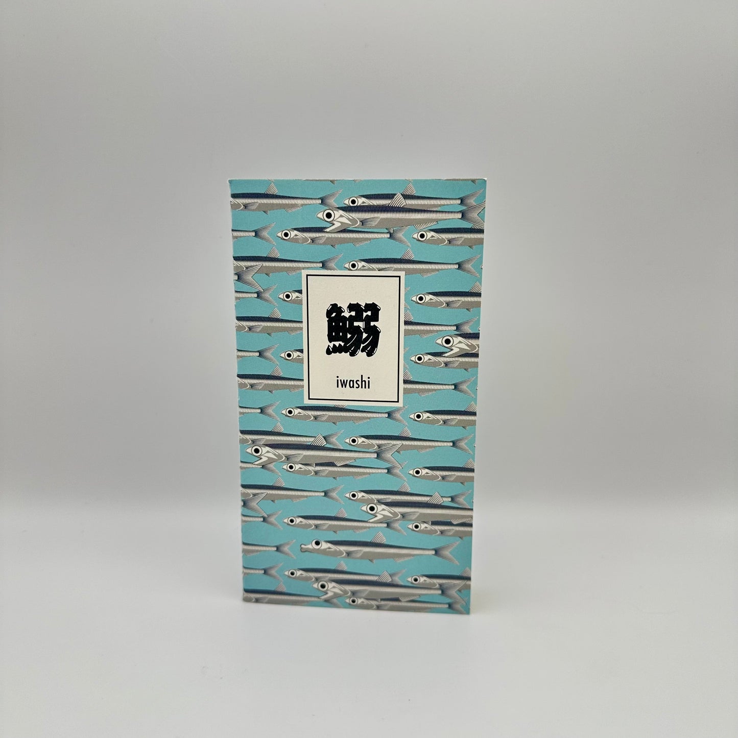 Notebook with blue background with silver sardines swimming. Text box in Japanese that reads "Iwashi"