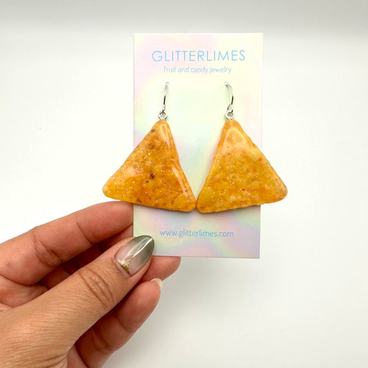 Tortilla chip earrings dipped in resin with glitter. On a card backing that says" Glitterlimes fruit and candy jewelry".