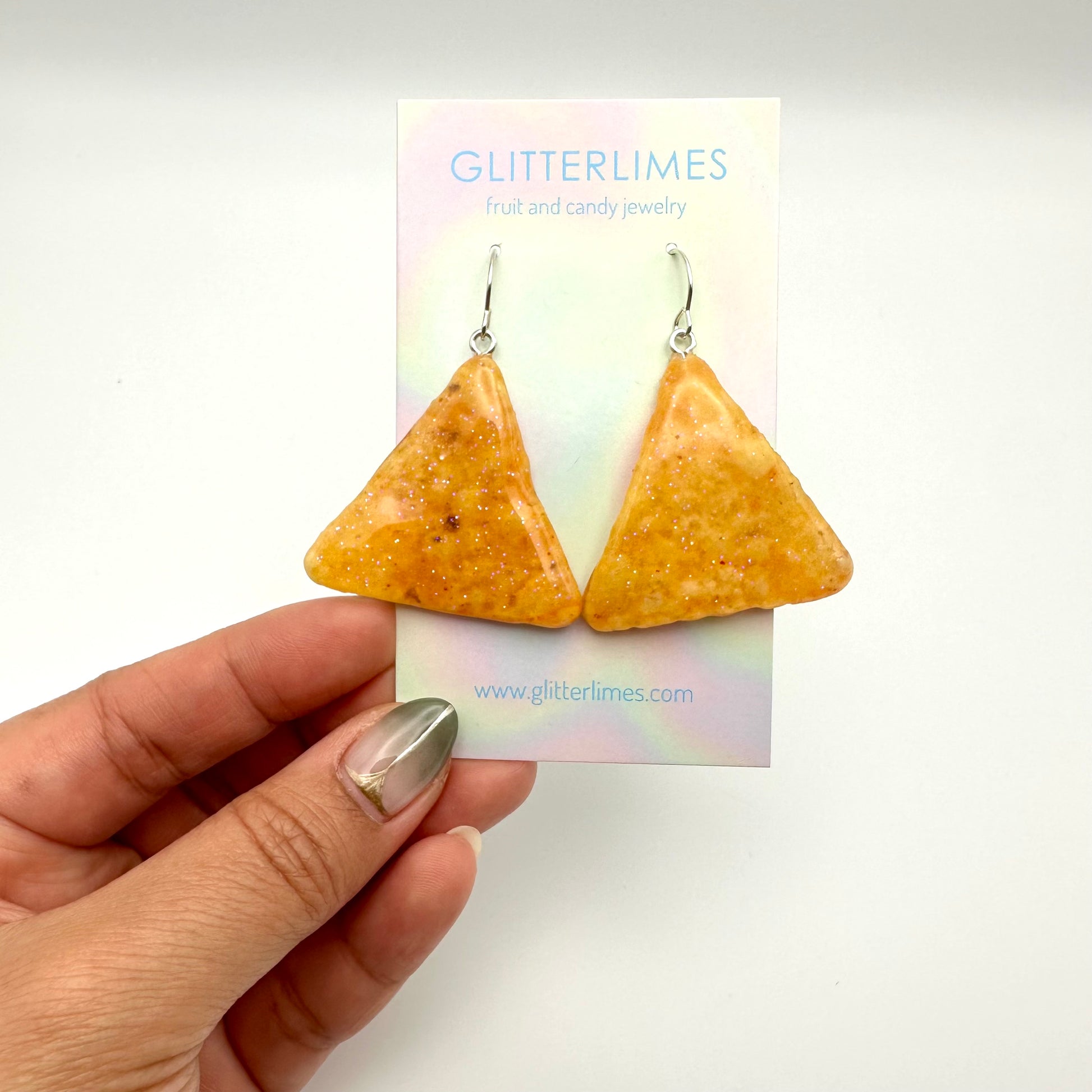 Tortilla chip earrings dipped in resin with glitter. On a card backing that says" Glitterlimes fruit and candy jewelry".