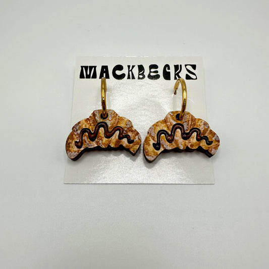 Chocolate croissant earrings with gold hoops. The card backing says Mackbecks.