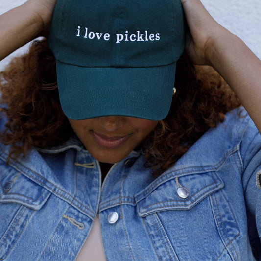Person wearing a green cap with 'i love pickles' text and a denim jacket.