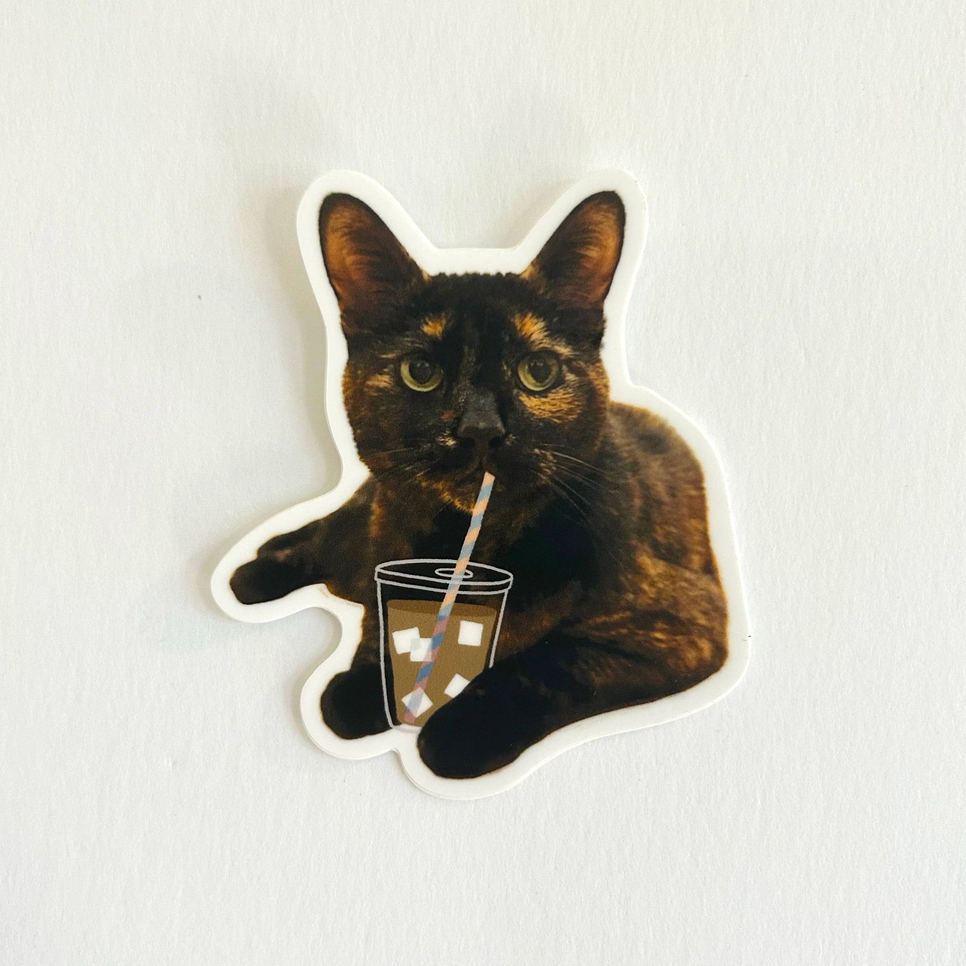 Sticker of a cat holding a coffee cup with a straw on a white background