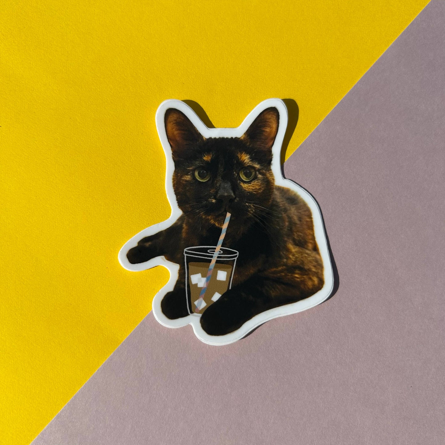Sticker of a cat holding a drink with a straw on a yellow and pink background