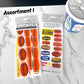 Two packages of food-themed stickers on a marble surface with a container partially visible.