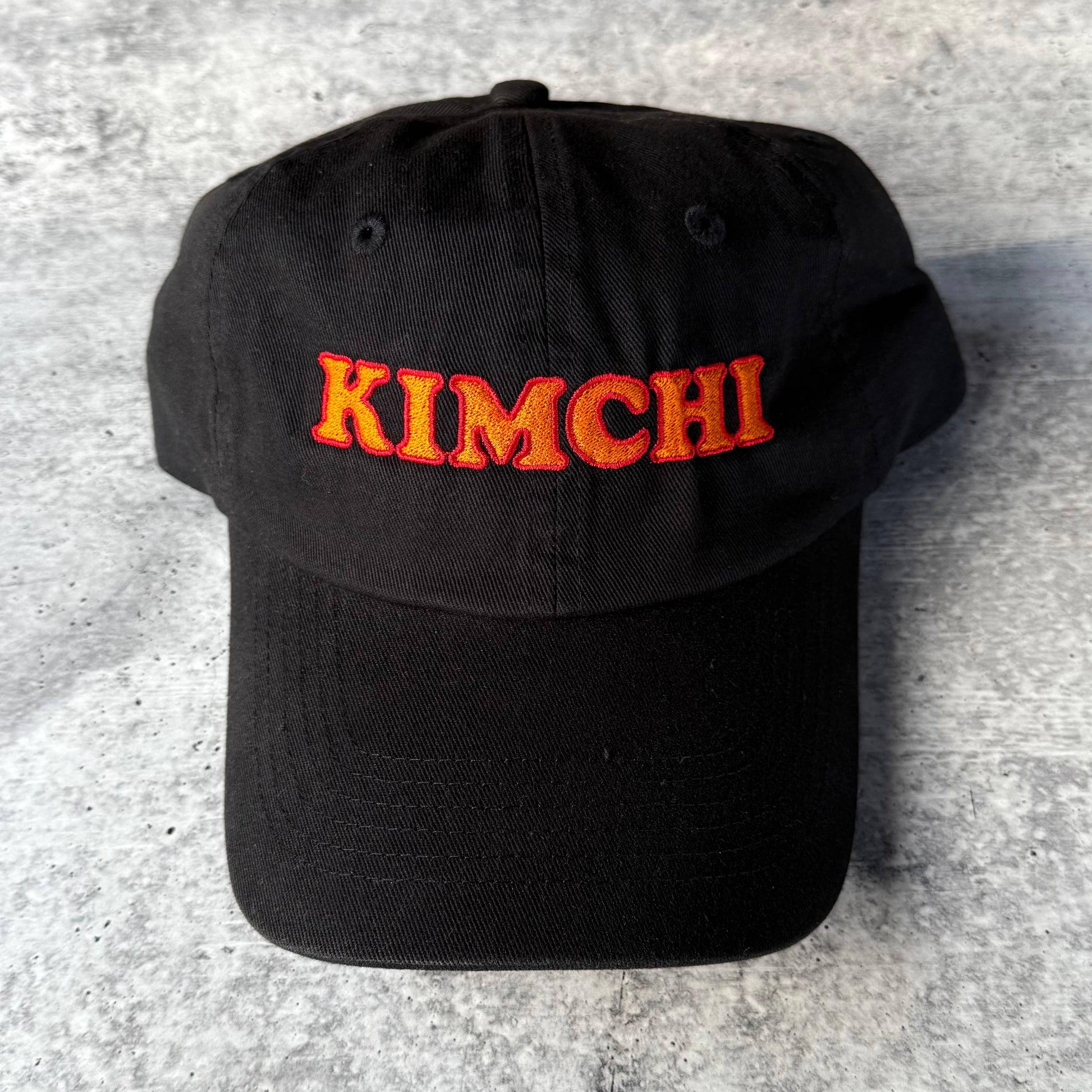 Black cap with 'KIMCHI' embroidered in orange on a gray surface