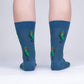 Blue crew socks with repeating pattern of an anthropomorphic pickle in red sunglasses, grinning and snapping his fingers like the cool guy he is. Shown on legs, back view.