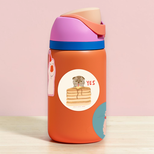 round sticker with illustrated cat licking pad of butter on a stack of pancakes and text just reads "yes" on water bottle 