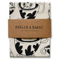 A folded cotton tea towel with a black and white coffee cup pattern, wrapped in a brown paper band that reads 'BADGER & BURKE 100% COTTON TEA TOWEL'.
