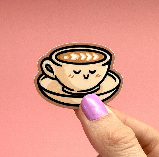 A cute cartoon coffee cup sticker held by a person's hand against a solid pink background.