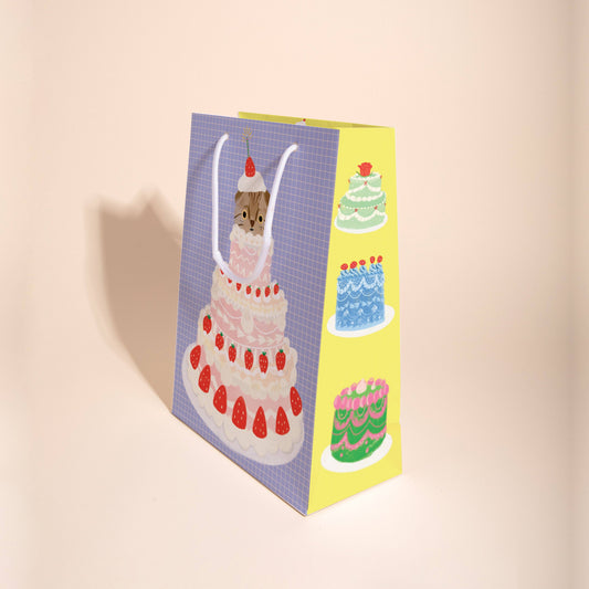 gift bag with tiered strawberry cake and a cat popping out of the top tier 