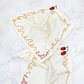 Two off-white napkins embroidered with a squiggly spaghetti noodle border, two red tomatoes, and "Let's Eat!" in red text. Shown on a marble surface.