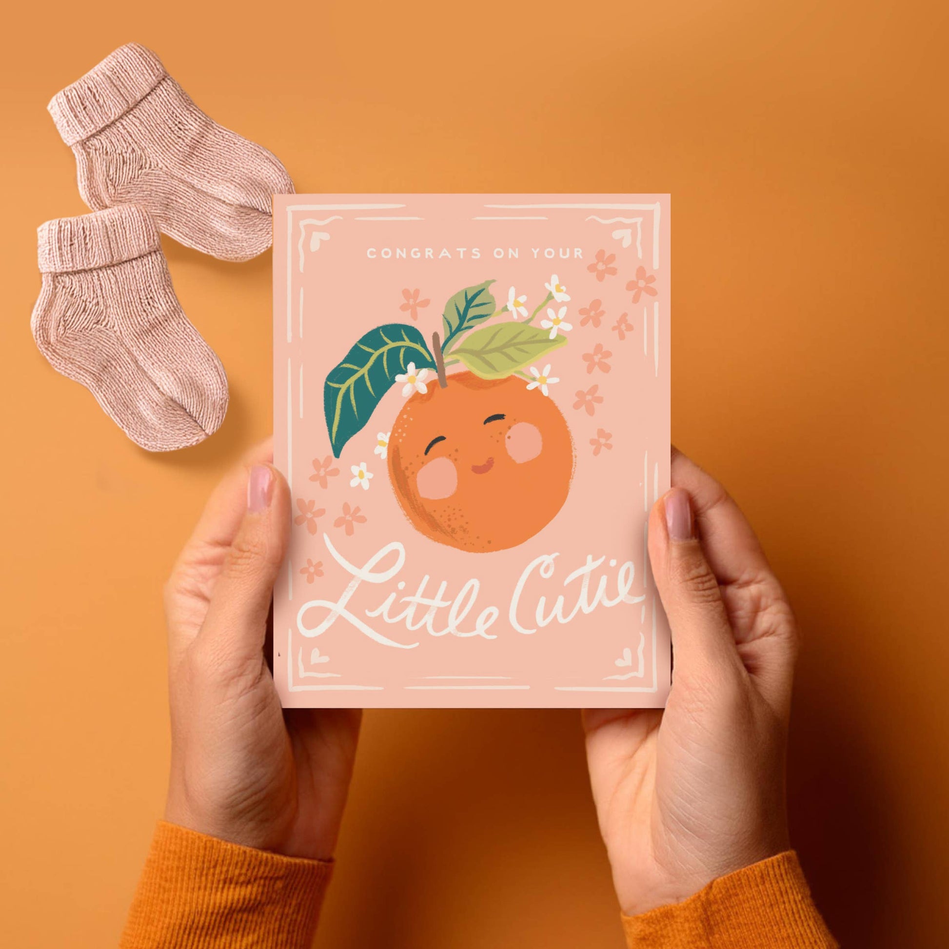 Person holding a baby shower card with an orange illustration and text on an orange background