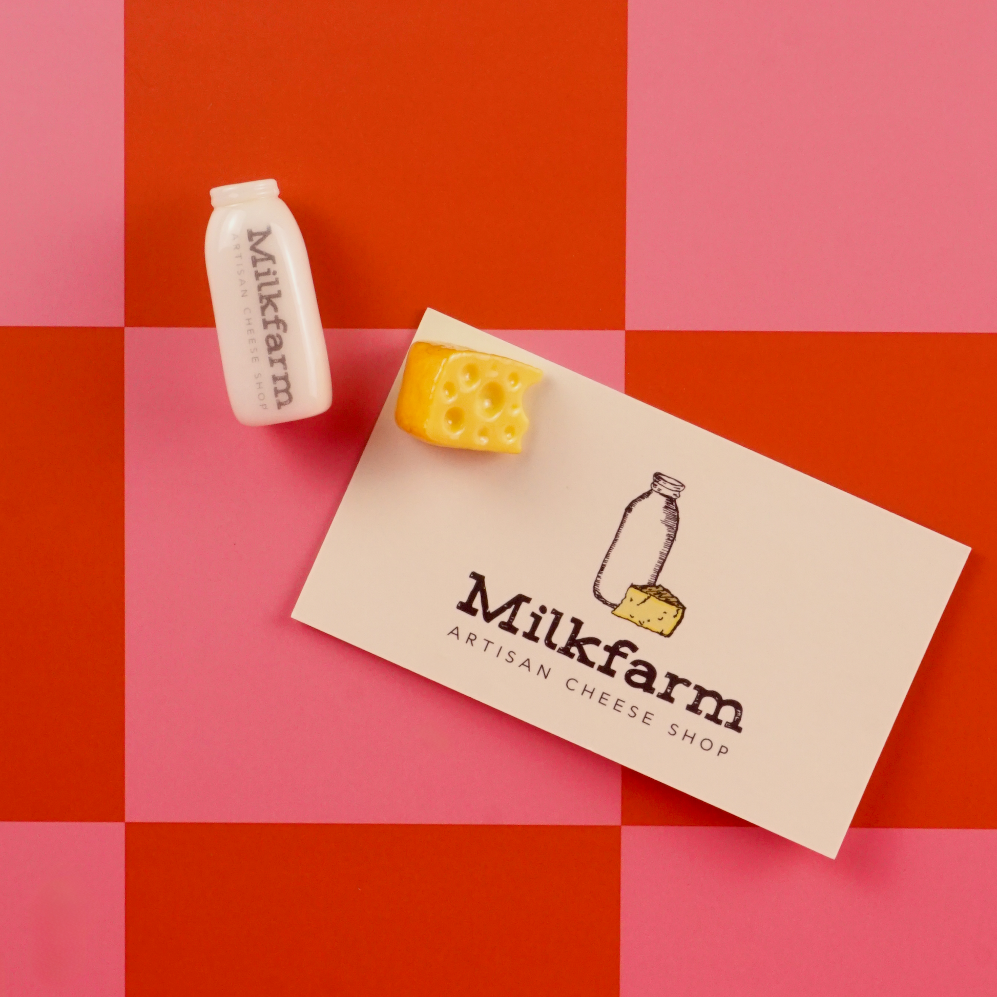 Milkfarm branding with a cheese block and bottle magnet on a red and pink checkered background