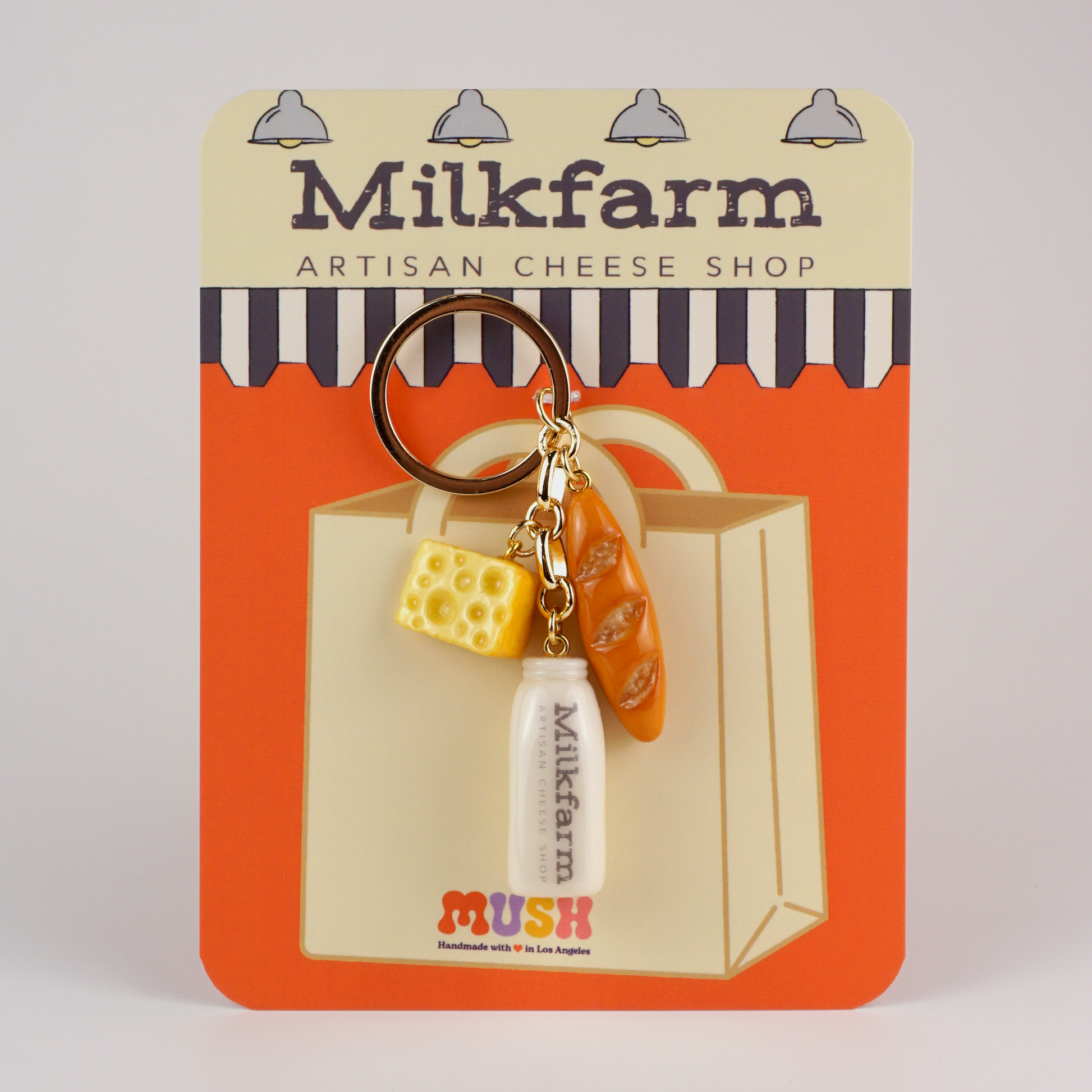 Keychain with charm s of cheese, milk bottle and baguette, on a Milkfarm packaging