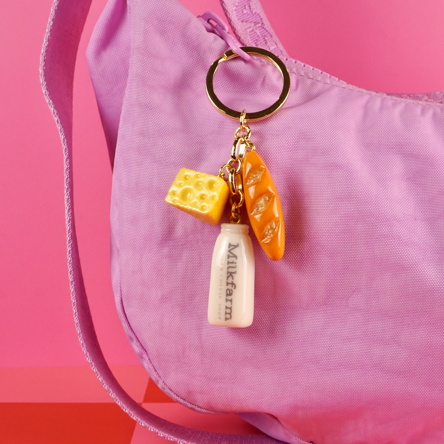 Keychain with bottle and cheese charms on a pink bag against a pink background