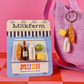 Milkfarm card featuring 5 magnets that look like snacks from the cheese shop. Purple bag with a keyring attached to it. The keyring as a milk botte, cheese and baguette charm.