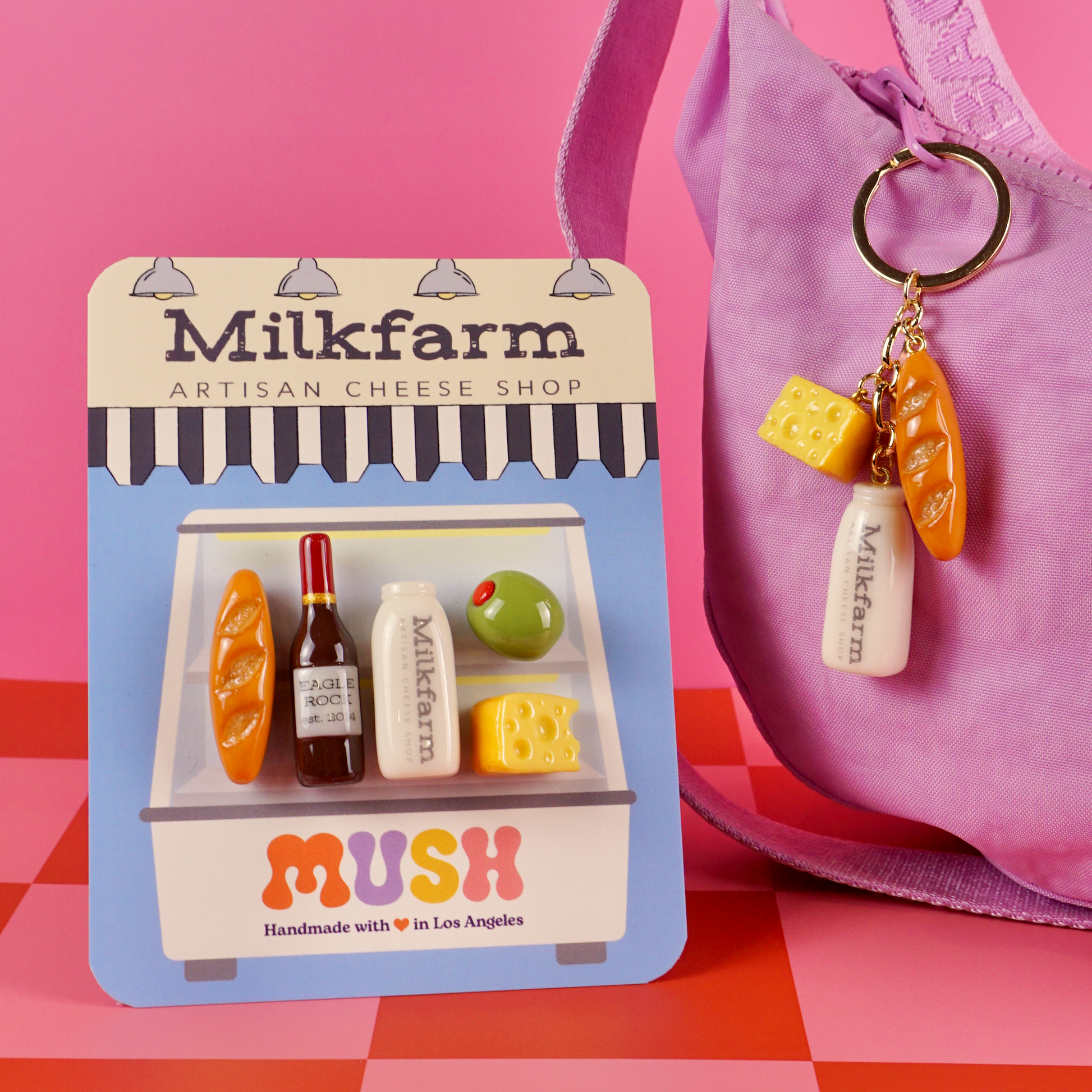 Milkfarm card featuring 5 magnets that look like snacks from the cheese shop. Purple bag with a keyring attached to it. The keyring as a milk botte, cheese and baguette charm.