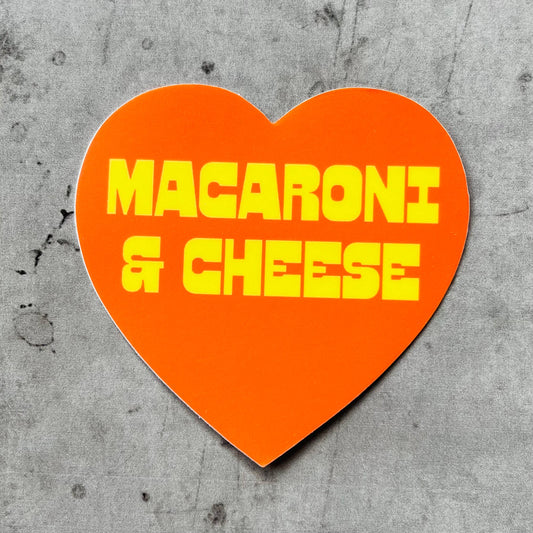 Orange, heart-shaped sticker with "macaroni & cheese" printed in quirky yellow font.