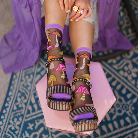 Person wearing colorful mushroom socks with platform sandals on a textured floor.