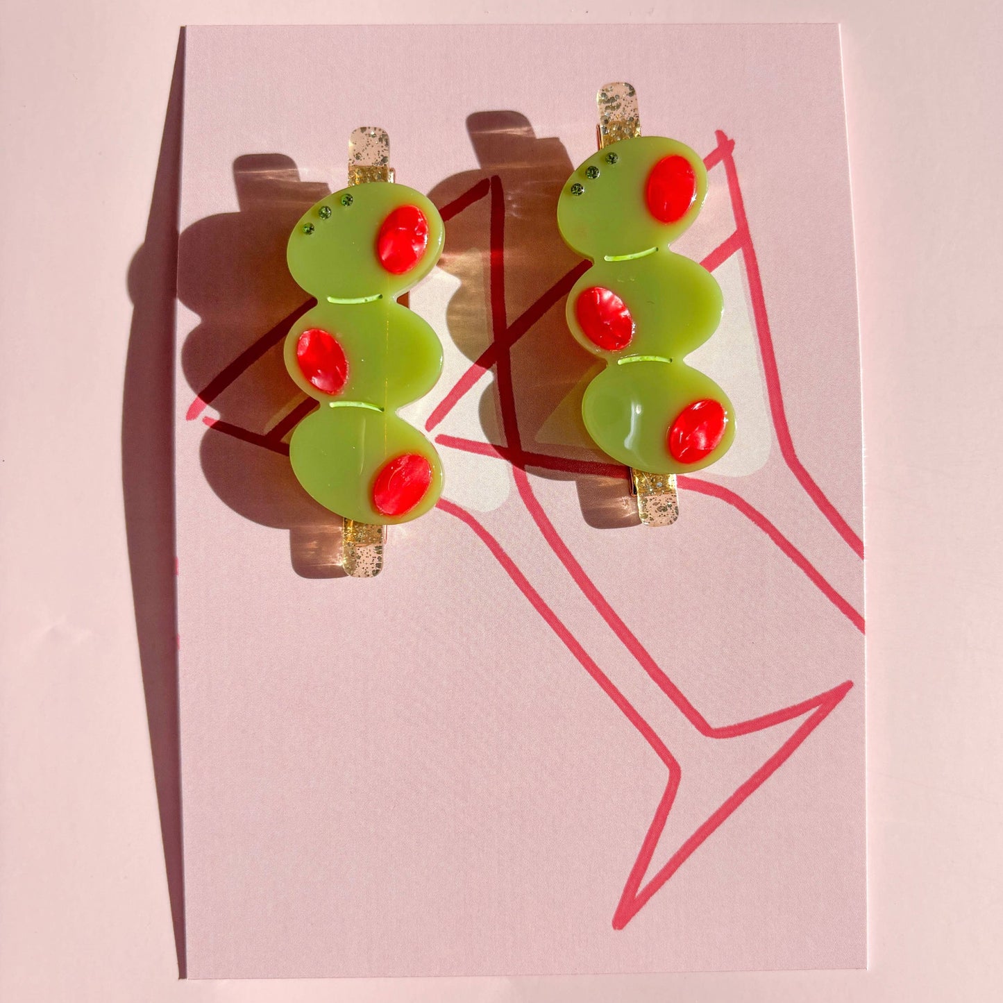 Pair of olive trio hair clips with green and red accents on a pink card