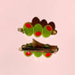 Two green olive trio hair clips with red dots on a pink background