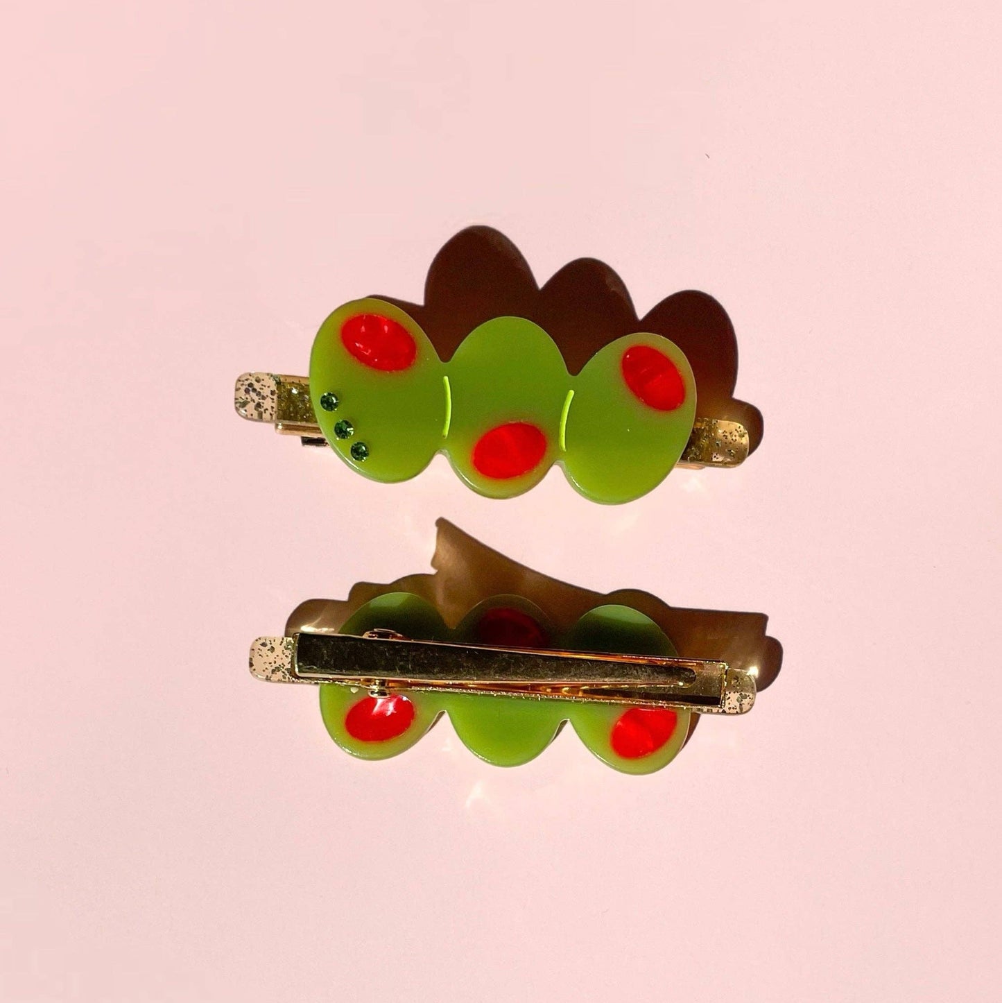 Two green olive trio hair clips with red dots on a pink background