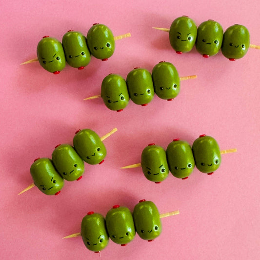 Green olive skewers shaped like caterpillars on a pink background