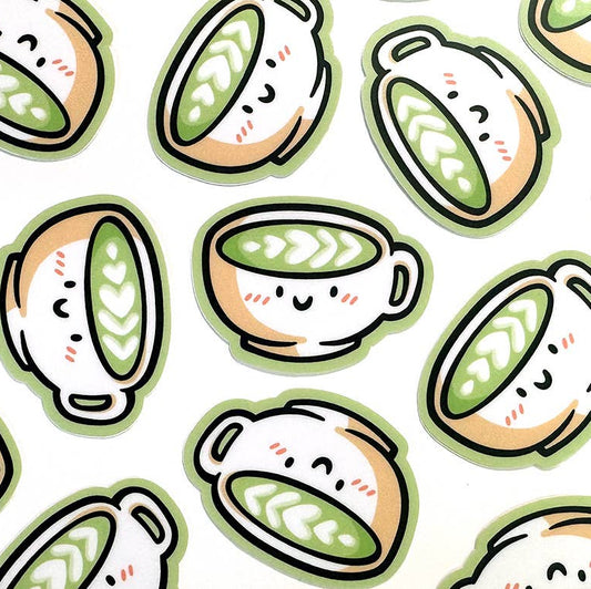 A repeating pattern of cute illustrated matcha lattes with smiling faces, shown on a white background.