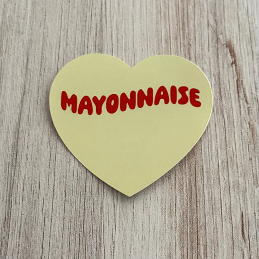 Heart-shaped green sign with 'Mayonnaise' in red text on a wooden surface