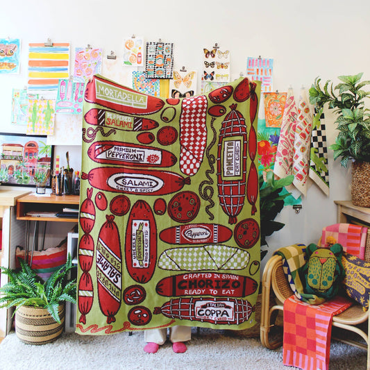 Someone holding a Meat Shop blanket in a work studio with a chair, art work, etc. 