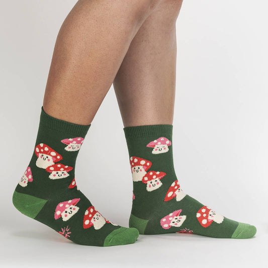 Green stocks with lime green heel and toe. Socks have smiling mushrooms with pink and red spotted caps. Model is wearing the socks and taking a step.