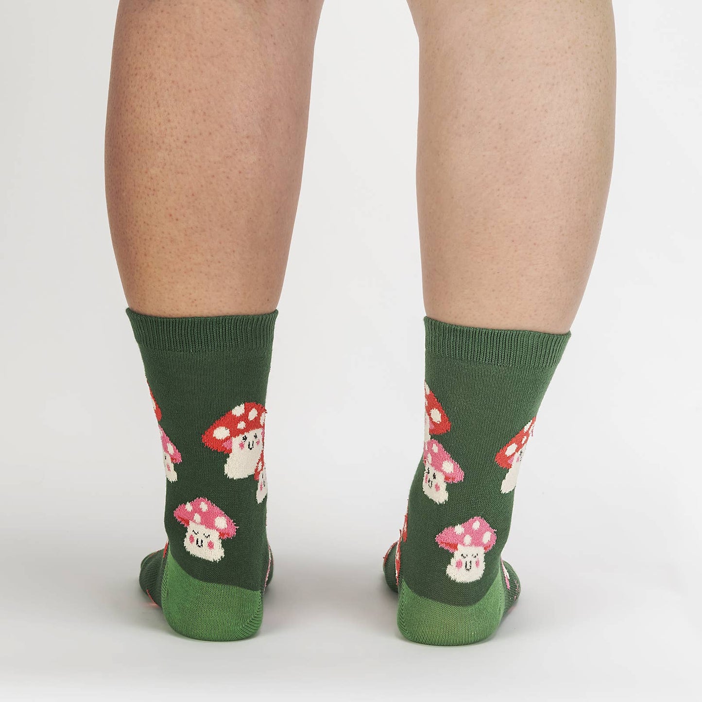 Green stocks with lime green heel and toe. Socks have smiling mushrooms with pink and red spotted caps. Model is standing while wearing the socks.