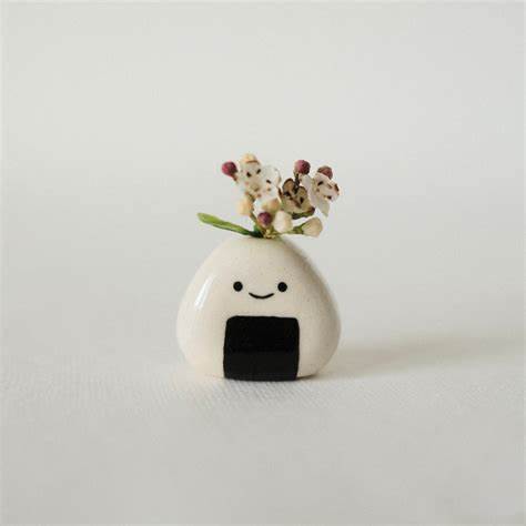 Photo of mini ceramic onigiri-shaped bud vase with a tiny smile. Shown with a tiny spray of flower buds inside vase.