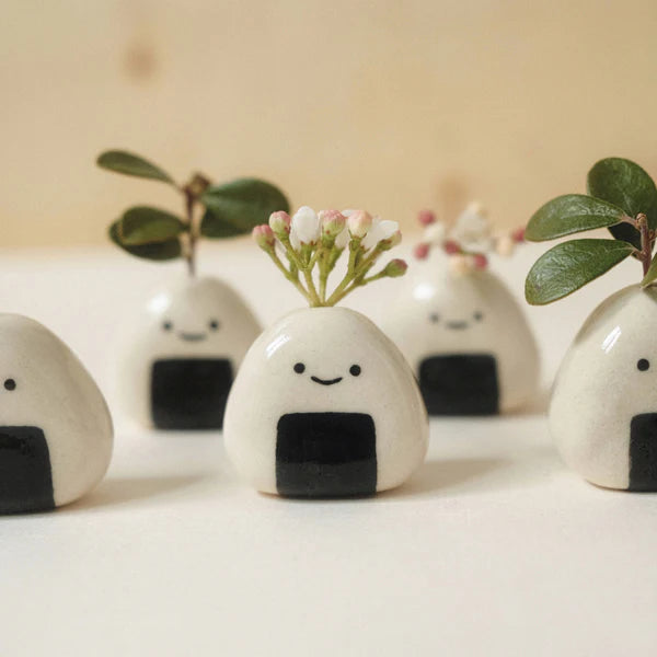Photo of five mini onigiri-shaped bud vases. Each vase has a single stem with tiny flowers or leaves.