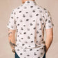 White button up shirt with tortoise buttons. Patterned with skulls, donuts, coffee and eyes. Male modeling the shirt from the back. 