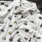 White button up shirt with tortoise buttons. Patterned with skulls, donuts, coffee and eyes. 